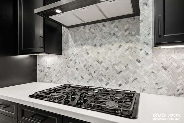 Black cabinets, herringbone backsplash, and quartz countertop with a gas cooktop in a Roseville kitchen remodel