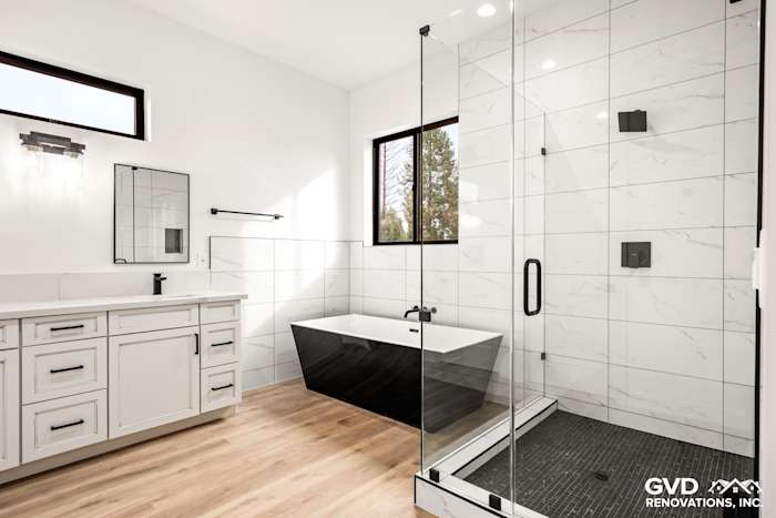 Modern bathroom featuring a freestanding black and white tub, glass-enclosed shower, and large windows for natural light