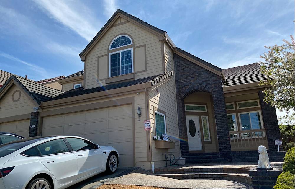 Old siding with beige tones, weathered brick accents, and outdated garage door