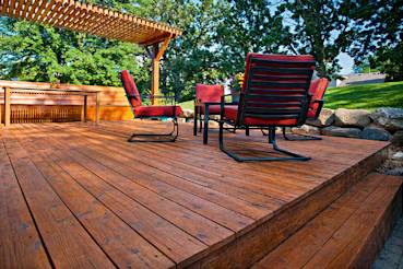 Custom-built wooden deck with red chairs, shaded by a pergola, surrounded by greenery