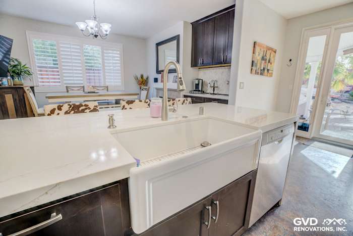 White farmhouse sink with quartz countertop, dark cabinets, and bright kitchen window in Roseville remodel