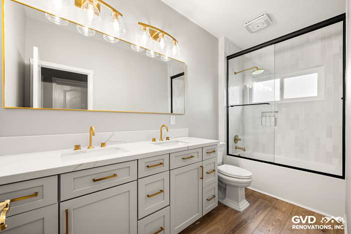 Modern guest bathroom with gray cabinetry, gold fixtures, sliding glass shower, and stylish lighting in El Dorado Hills
