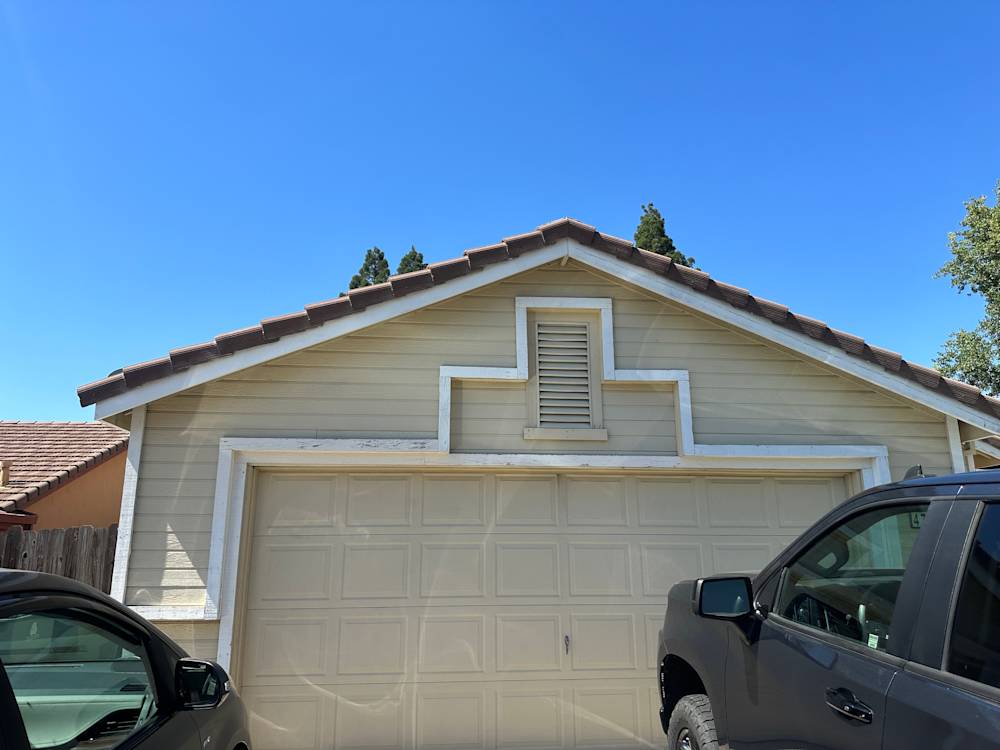 A faded yellow house with a tiled roof and garage, surrounded by greenery in Sacramento
