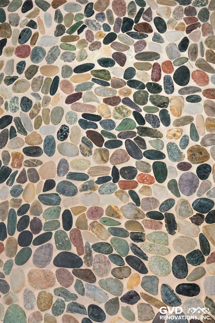 Close-up of a natural stone mosaic floor in a renovated bathroom, featuring various earth tones and textures