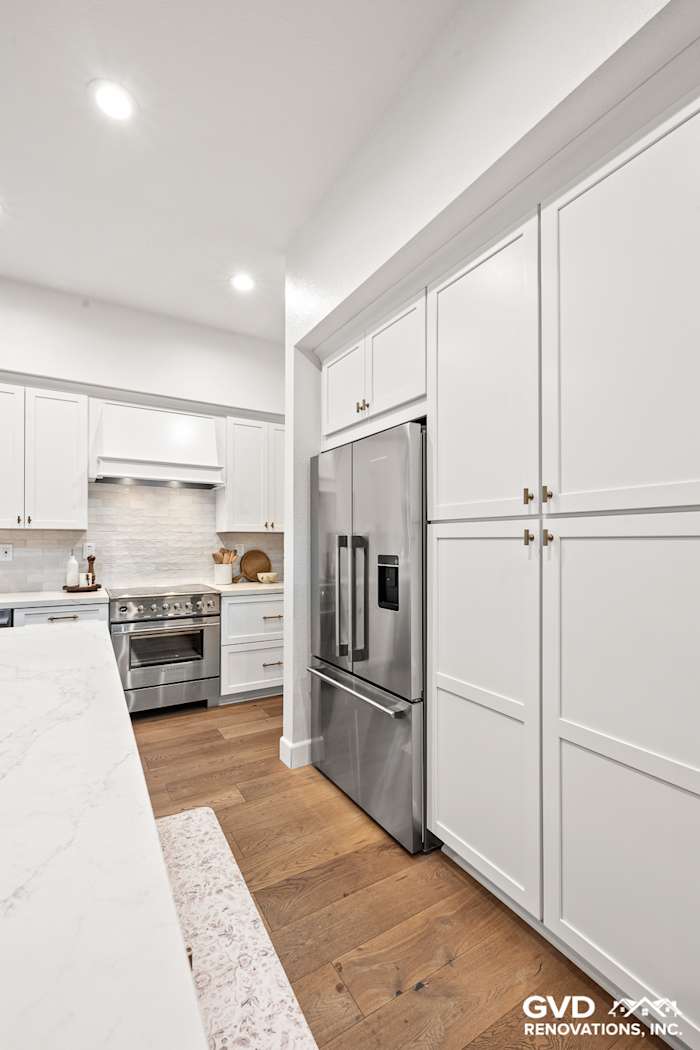 Modern kitchen with white Waypoint cabinets, a sleek stainless steel refrigerator, and bronzed mitered edge countertops