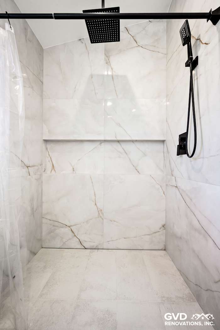 Modern shower featuring large marble tiles, rain showerhead, and sleek black fixtures in a remodeled bathroom