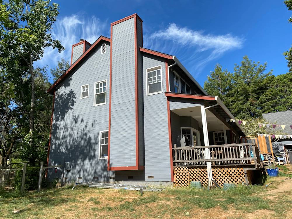 Gray two-story home with red trim and wooden deck in Sacramento's sunny landscape