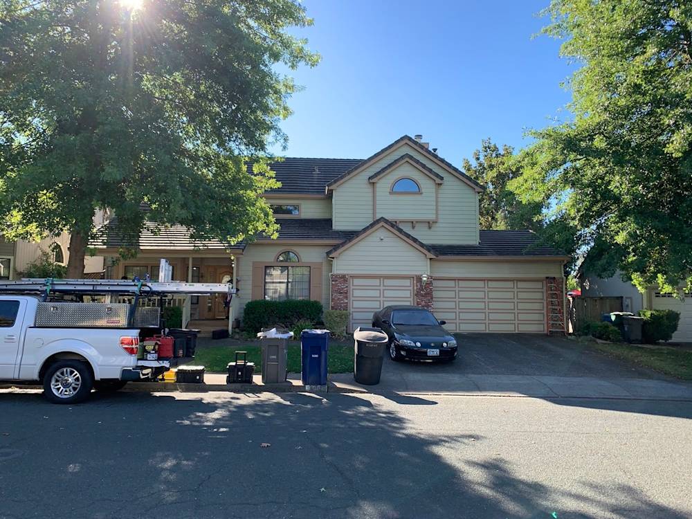 Two-story home in Sacramento with light green siding and a three-car garage, surrounded by trees