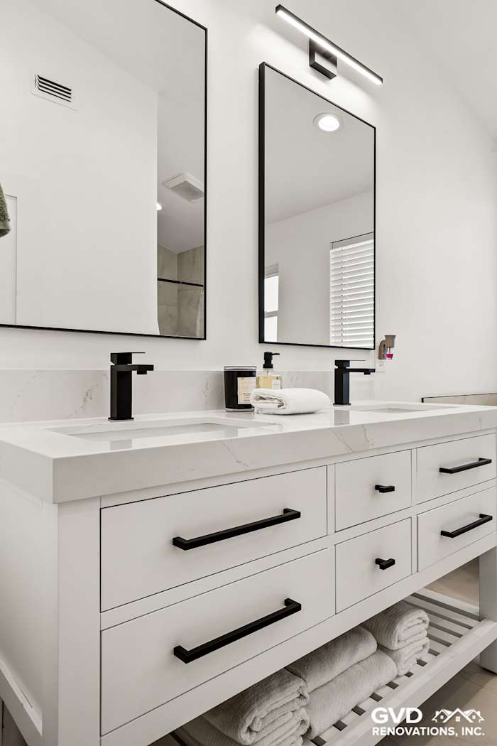 Modern bathroom with dual vanities, sleek black fixtures, and large mirrors over white countertops