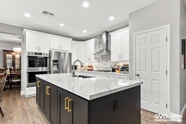 Modern kitchen featuring Cambria countertops, custom white cabinets, and a dark island with gold hardware in Roseville