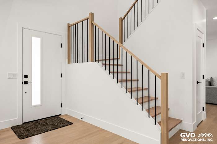 Modern staircase with wooden treads, black railings, and bright white walls in remodeled entryway