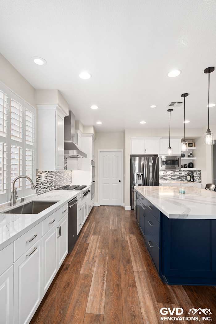 Modern kitchen in El Dorado Hills featuring white cabinets, dark blue island, and quartz countertops with pendant lighting