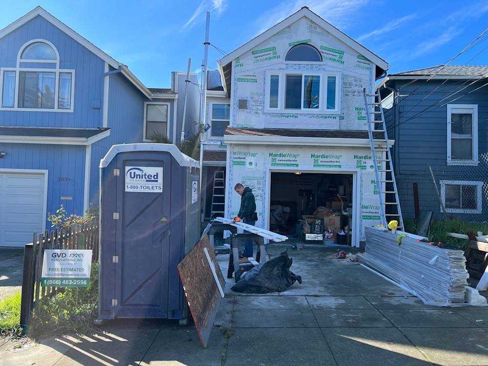 Residential exterior with construction materials, blue siding, and portable restroom in Sacramento