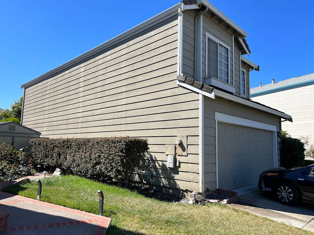 Side view of a home exterior in Sacramento with beige siding and overgrown shrubs