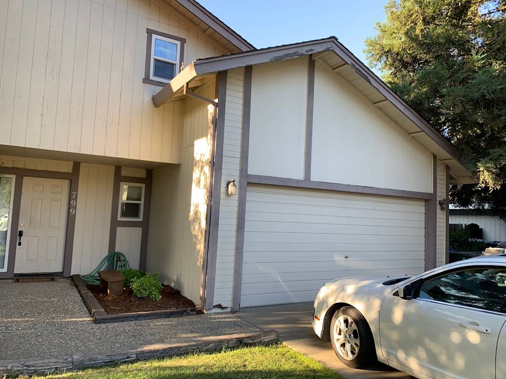 Dated exterior of a home in Sacramento, featuring beige siding and gray trim with a concrete driveway