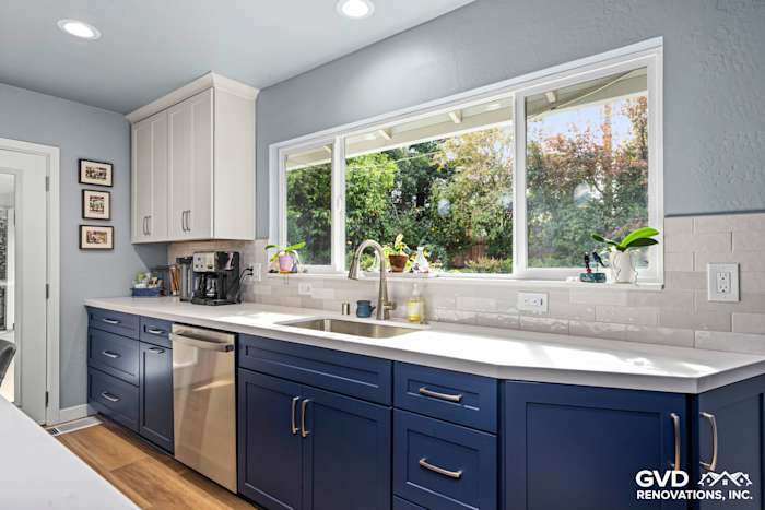 Modern kitchen with blue and white cabinetry, quartz countertop, and large window overlooking greenery