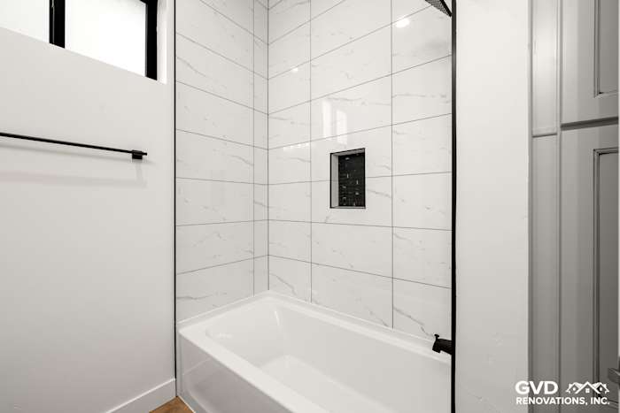 Modern bathroom featuring a white bathtub, marble-patterned tiles, and sleek black fixtures