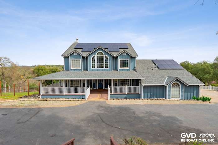 Modern blue James Hardie siding on a large home with solar panels and a wraparound porch in Shingle Springs, CA