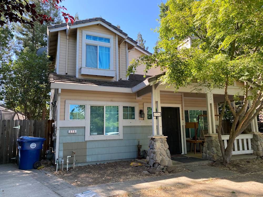 Two-story home exterior with beige siding, stone accents, and lush trees in Sacramento