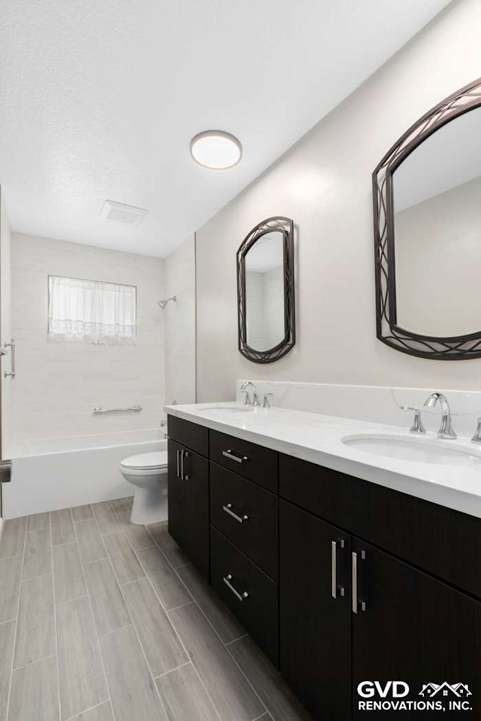Modern master bathroom remodel in Rocklin featuring sleek dark cabinetry, dual mirrors, and neutral tiling