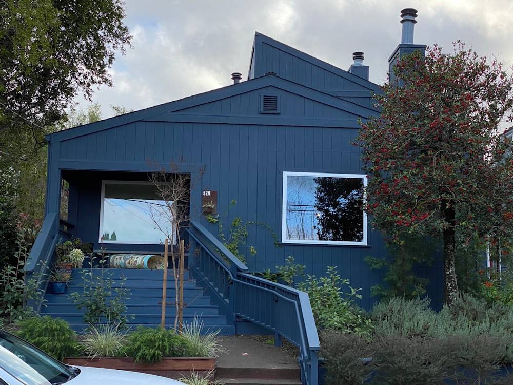 Blue exterior home with prominent window, lush greenery, and modern architectural lines in Sacramento