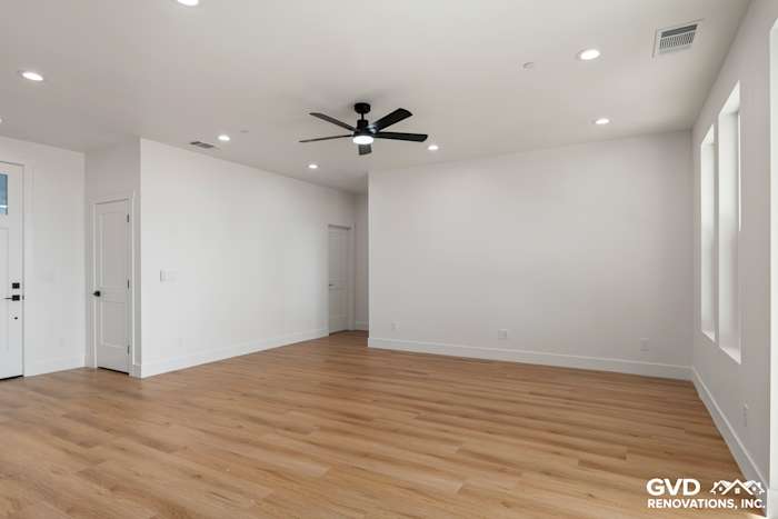 Spacious living room with light wood flooring, white walls, ceiling fan, and large windows in new construction home