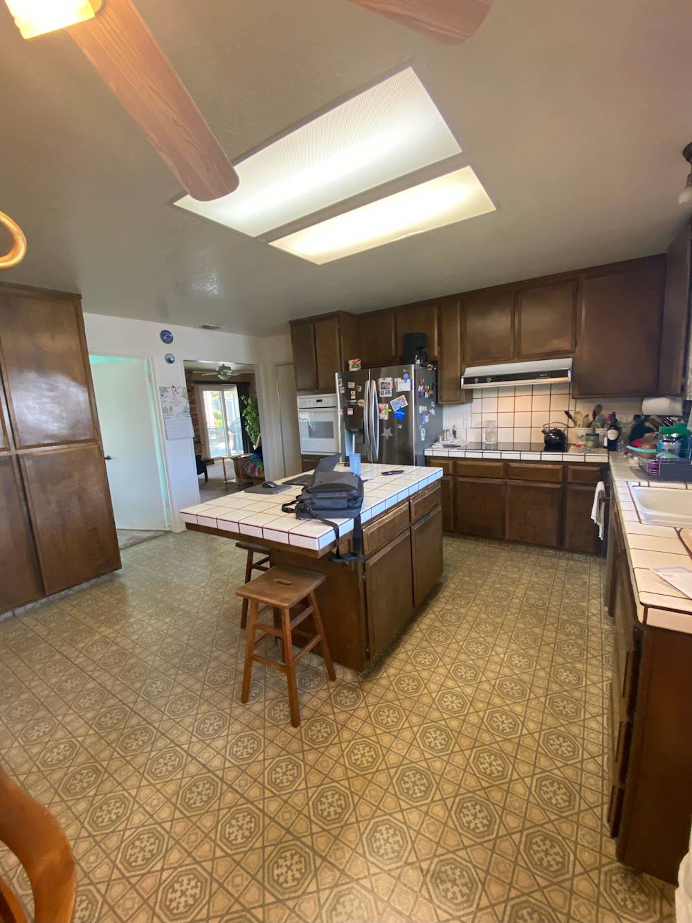 Spacious kitchen with dark wood cabinets, white tiled countertops, and patterned linoleum flooring in Sacramento