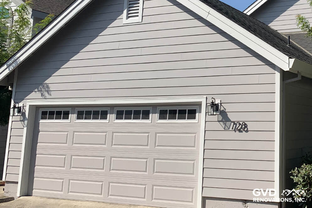 Fresh gray siding with decorative garage door, modern lighting fixtures
