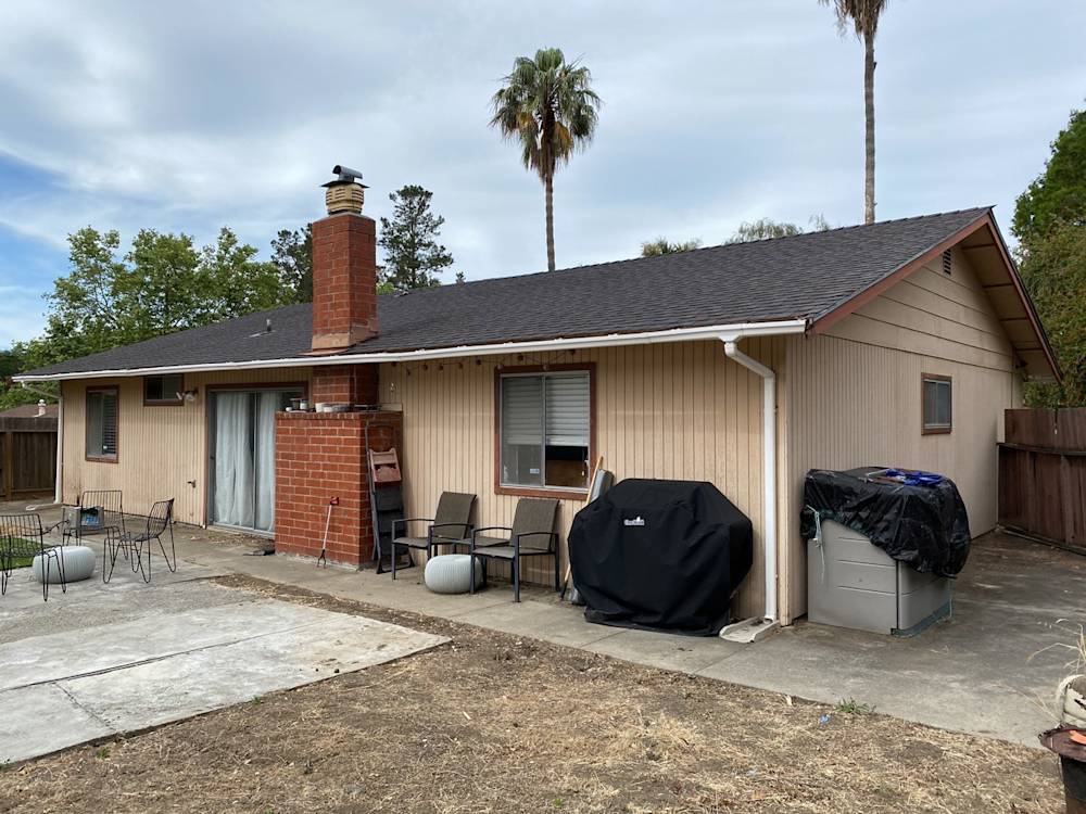 Outdated backyard of a Mendocino home featuring a concrete patio and red brick chimney