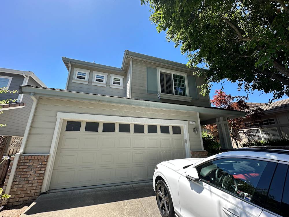 Two-story gray home with a brick accent, large garage door, and shaded front yard in Sacramento