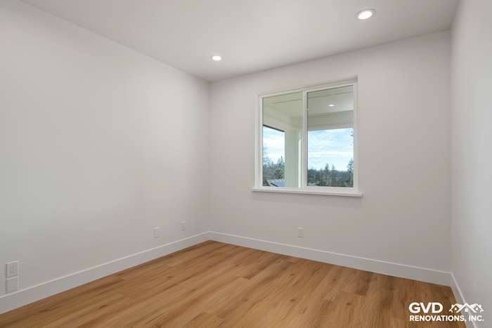 Bright empty room with white walls, large window, and warm wood flooring in a new construction home