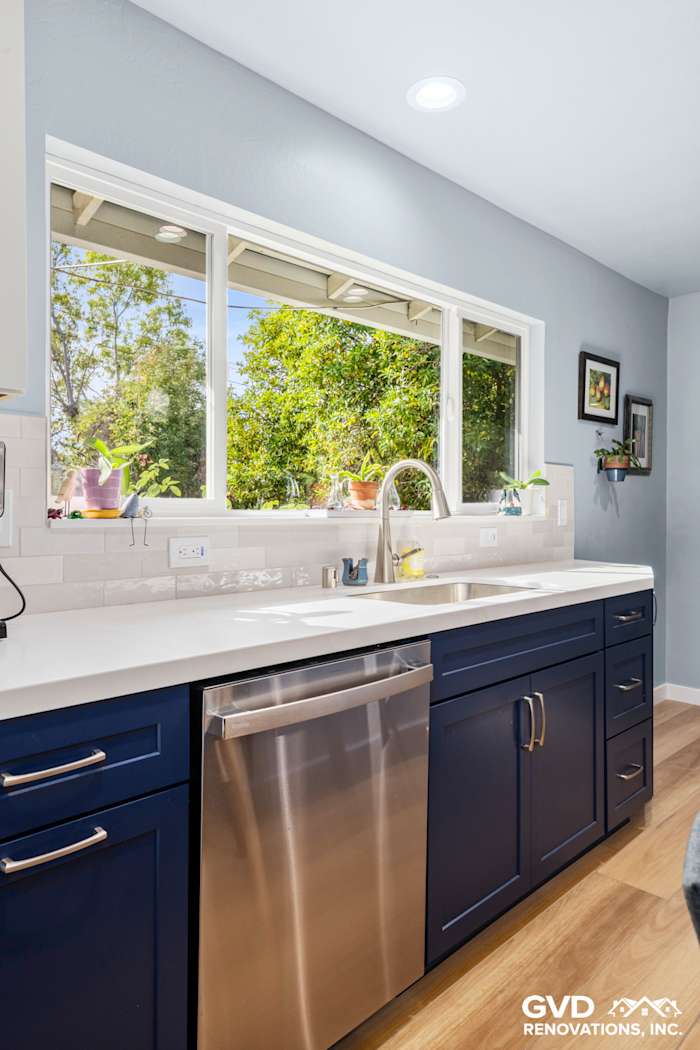 Modern kitchen with navy blue cabinets, white quartz countertop, and large window for natural light