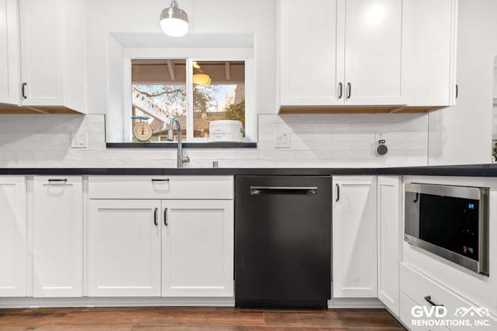 Modern white shaker kitchen with black appliances, quartz countertops, and wooden flooring in Loomis, CA