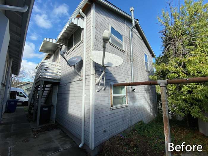 Before image of a home exterior featuring old gray siding, no windows, and satellite dishes in Rio Vista