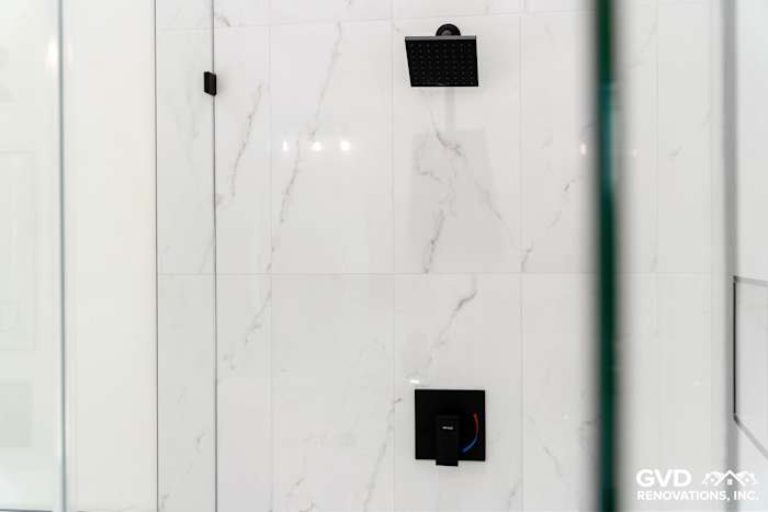 Black rainfall showerhead above sleek marble wall, featuring modern handles in a custom bathroom design