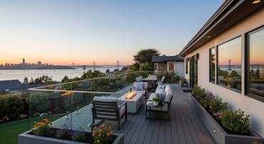 Modern deck with glass railing overlooking the bay, featuring cozy seating and vibrant flower planters