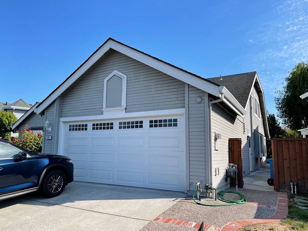 Single-story gray house with a white garage, driveway, and landscaped garden in Sacramento