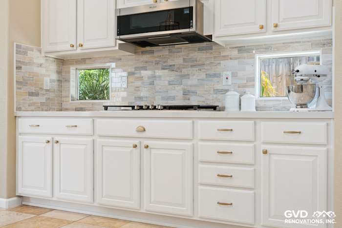 Bright kitchen featuring white cabinetry, stone backsplash, quartz countertop, and stainless steel appliances
