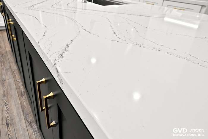 Close-up of Cambria quartz countertop with veining, featuring modern black cabinets and gold hardware