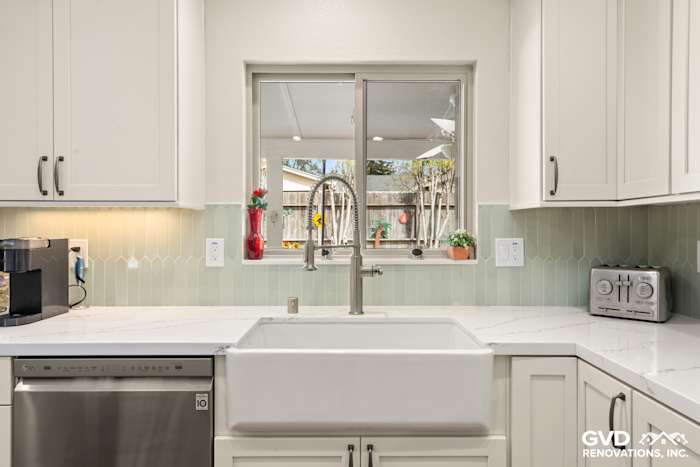 Modern kitchen with white cabinets, farmhouse sink, quartz countertops, and green herringbone backsplash in Carmichael
