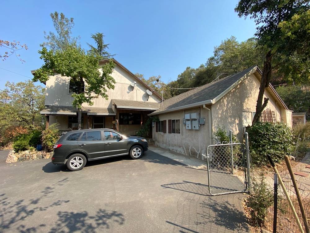 A weathered home exterior in Northern California, featuring a concrete driveway and overgrown landscaping