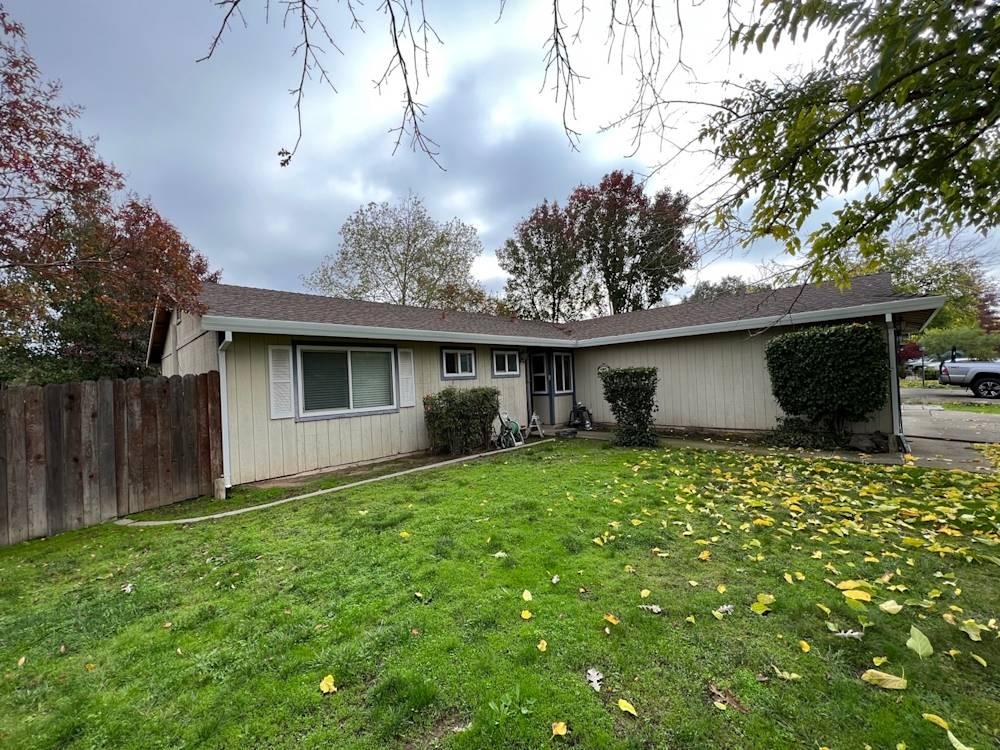 Single-story house with light siding, green lawn, and mature trees in Sacramento area