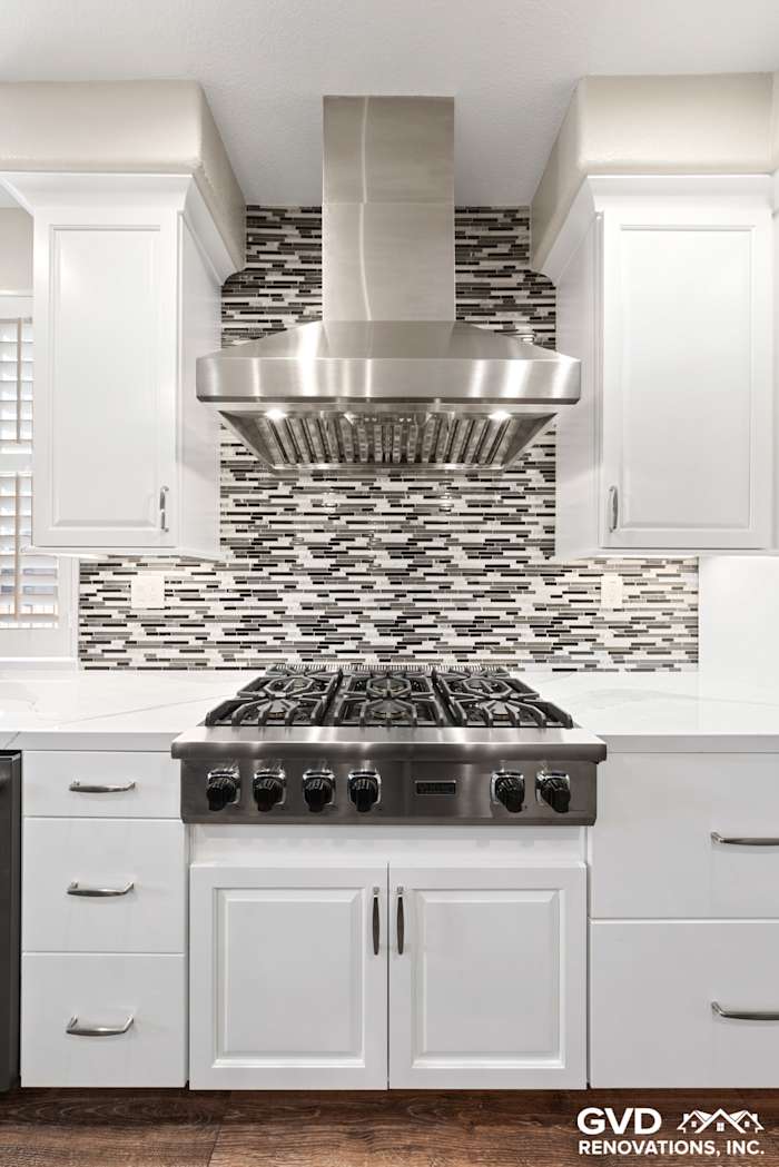 Modern kitchen featuring stainless steel range hood, gray mosaic backsplash, and white cabinetry in El Dorado Hills