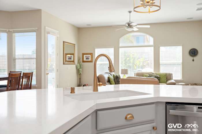 Bright kitchen featuring a white quartz countertop, gold faucet, and open floor plan to living area