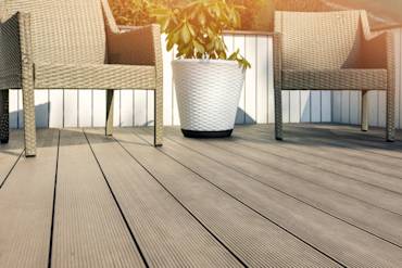 Light-colored composite deck with two woven chairs and a potted plant, creating a cozy outdoor space