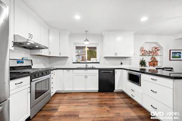 Modern kitchen with white shaker cabinets, black countertop, stainless steel appliances, and wood flooring in Sacramento