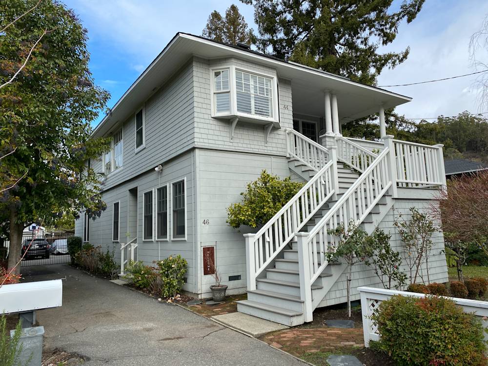 Two-story gray house in Tamalpais, featuring white railings, greenery, and a stone walkway