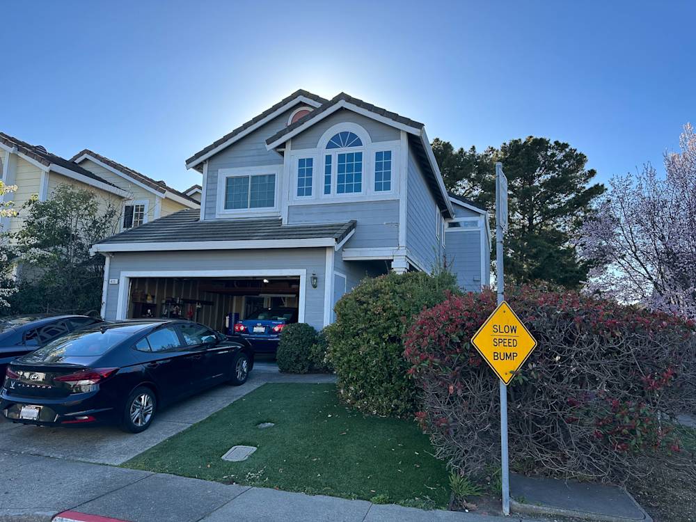 Two-story light blue home in Sacramento with green lawn and blooming bushes