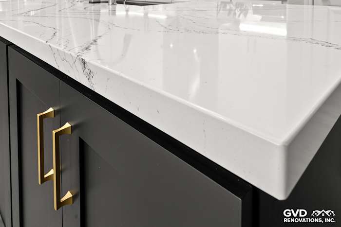 Close-up of Cambria custom countertops featuring elegant marbling and black cabinetry with gold handles in a kitchen remodel