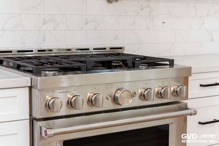 Professional-grade stainless steel gas range with multiple burners and marble backsplash in a custom kitchen